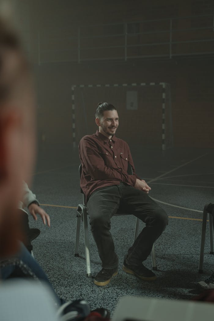 Adults engaged in a group therapy session inside a dimly lit, smoky room.